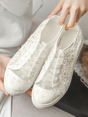 Chaussures de mariée plates ivoire à bout rond ornées de perles et lacées style baskets décontractées.