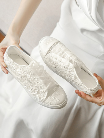 Chaussures de mariée plates ivoire à bout rond ornées de perles et lacées style baskets décontractées.